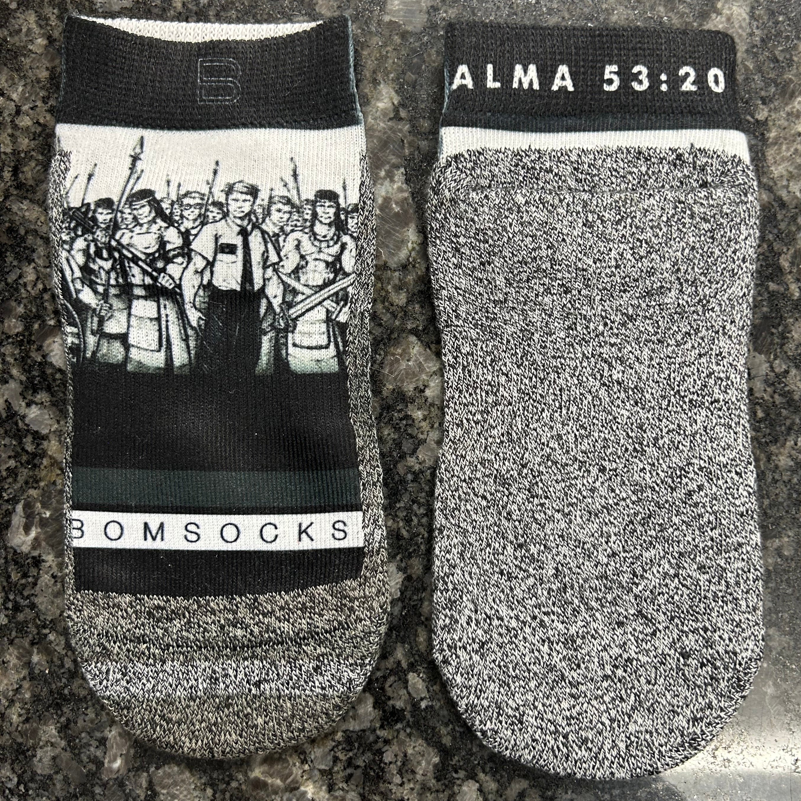 A pair of low-cut, gray and black socks with a black cuff featuring white text that reads 'ALMA 53:20'.